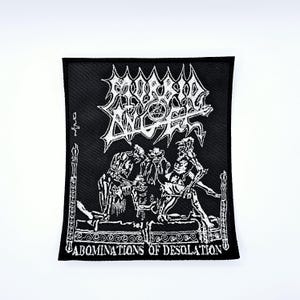 Puede incluir: Parche cuadrado negro con texto e imágenes bordadas en blanco. El parche presenta el nombre de la banda "MORBID ANGEL" sobre una ilustración gráfica de figuras en una cama. El texto "ABOMINATIONS OF DESOLATION" está en la parte inferior.