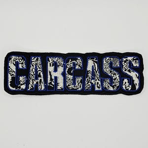 以下が含まれることがあります： 太いブロック体で「CARCASS」という文字が刺繍された長方形のワッペン。文字は白と黒のマーブル模様やテクスチャで埋め尽くされており、黒い背景に対して鮮やかな青い糸で縁取りが施されています。