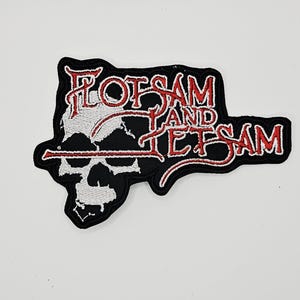 Puede incluir: Un parche bordado que presenta el texto Flotsam and Jetsam en hilo rojo con un contorno blanco. El diseño incluye un gráfico de calavera blanca sobre un fondo negro, con el texto posicionado sobre la calavera y extendiéndose hacia la derecha.