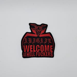 Può includere: Toppa ricamata nera e rossa con la scritta "ABIGAIL WELCOME ALL HELL FUCKERS". La toppa presenta un disegno di testa di capra cornuta rossa nella parte superiore.