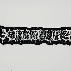 Puede incluir: Un parche bordado rectangular con fondo negro y texto blanco en una fuente gótica estilizada, dentada y desgastada. Los bordes del parche son irregulares y siguen el contorno de las letras, creando un diseño de alto contraste y llamativo.