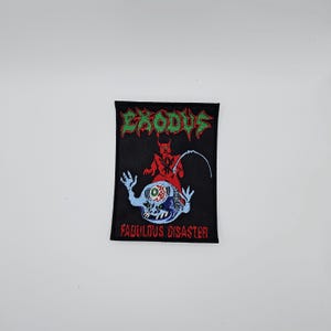 May include: Black embroidered patch featuring the word "EXODUS" in green, a red devil figure, and a blue creature with a single eye. The text "FABULOUS DISASTER" is below the creature. The patch is rectangular.