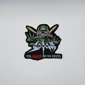May include: Embroidered patch with a green and black design of a soldier in a gas mask and helmet. The patch features the band name "SODOM" and the phrase "'TIL DEATH DO US UNITE" in red and white.