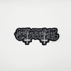 Peut inclure: Écusson noir brodé avec des coutures blanches. Le patch présente le mot "BRUTALITY" dans une police stylisée, avec deux croix inversées. Le patch est rectangulaire avec un contour incurvé.