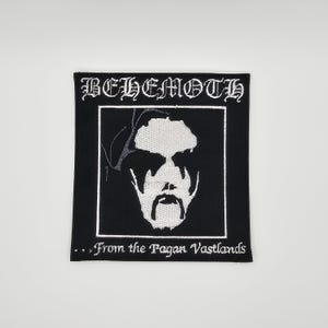 May include: Black and white embroidered patch featuring the word "BEHEMOTH" in gothic lettering above a stylized face. The text "...From the Pagan Vastlands" is below the face. The patch is square.