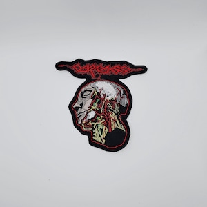 May include: Embroidered patch featuring a profile of a human head with exposed internal anatomy. The design includes red and green details on a black background, with the word "CARCASS" in red above the head.