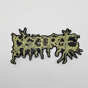 May include: Black patch with the word "DEATH" in a stylized, yellow, distressed font. The patch has a black border and a white background. The design has a grunge aesthetic.