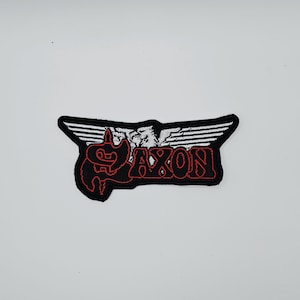 以下が含まれることがあります： 黒と赤の刺繍パッチ。スタイリッシュなフォントで「AXON」の文字がデザインされています。翼のデザインと生き物のグラフィックが特徴です。ジャケットやバッグに最適です。