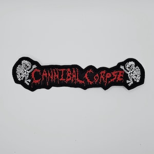 Op de afbeelding: Een zwart geborduurd embleem met de tekst "CANNIBAL CORPSE" in rode, gestileerde letters. De patch heeft een zwarte rand en witte skeletfiguren aan elk uiteinde. De patch is rechthoekig van vorm.