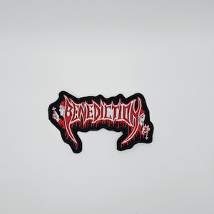 Op de afbeelding: Een zwart embleem met het woord "BENEDICTION" in rode, gestileerde gotische letters. Het embleem heeft een rode rand met een druipend bloedeffect en kleine decoratieve elementen. Voor kleding of tassen.