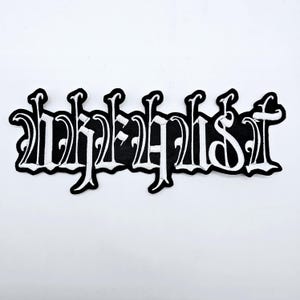 Puede incluir: Parche bordado en blanco y negro con la palabra "Alphabetist" en fuente gótica. El parche tiene un borde negro y el texto es blanco. Adecuado para ropa o accesorios.