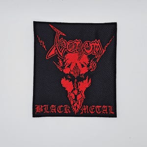 May include: Black embroidered patch featuring the word "Venom" in red, stylized text above a red demonic face. The words "BLACK METAL" are embroidered in red below the image. The patch is square and has a black background.
