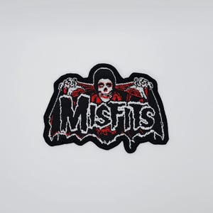 Op de afbeelding: Geborduurde patch met het woord "MISFITS" in wit, met een rood-zwarte schedelafbeelding. De patch heeft een zwarte rand en is bedoeld voor kleding of accessoires.