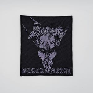 May include: Black rectangular patch with the word "Venom" in a stylized, gray font above a gray demonic face. The text "BLACK METAL" is below the face in a similar font.