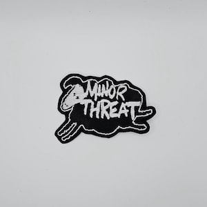 Peut inclure: Écusson brodé noir et blanc représentant un mouton courant avec l'inscription "MINOR THREAT" en lettres manuscrites blanches. Le patch a un fond noir et des coutures blanches.