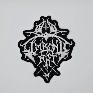 May include: Black and white embroidered patch featuring the words "ABSENT ART" in a gothic style font. The patch has an ornate shape with decorative elements, including crosses and stylized designs.