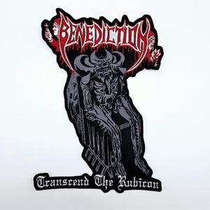 Puede incluir: Parche bordado con la palabra "BENEDICTION" en fuente roja goteante sobre una ilustración detallada en negro y gris de una figura esquelética. El texto "Transcend The Rubicon" está debajo.