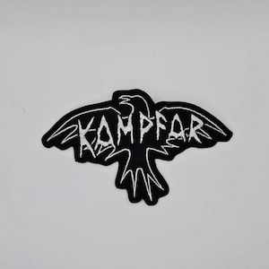 May include: Black and white embroidered patch featuring a stylized raven with outstretched wings. The word "KAMPFAR" is embroidered in white across the raven's body. The patch is likely designed for application on clothing or accessories.