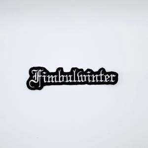 Könnte beinhalten: Ein schwarzer, gestickter Aufnäher mit dem Wort "Fimbulwinter" in gotischer Schrift. Der Aufnäher hat einen schwarzen Rand und ist vor einem weißen Hintergrund platziert. Der Text ist weiß.