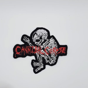 Könnte beinhalten: Gestickter Aufnäher mit einem weißen Skelett auf schwarzem Hintergrund. Der Aufnäher zeigt den roten Text "CANNIBAL CORPSE" in einer stilisierten Schriftart. Geeignet zur Individualisierung von Kleidung oder Accessoires.