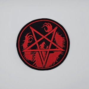 Puede incluir: Parche redondo negro con un diseño de pentagrama rojo. El pentagrama está rodeado por un círculo rojo y presenta manos y figuras rojas estilizadas. El parche es probablemente para ropa o accesorios.
