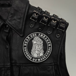 Può includere: Giubbotto in pelle nera con una grande toppa ricamata che presenta un ritratto di Vlad l'Impalatore, con il testo "Vlad l'Impalatore, Voivoda di Valacchia". Il giubbotto ha più fibbie sulla spalla.