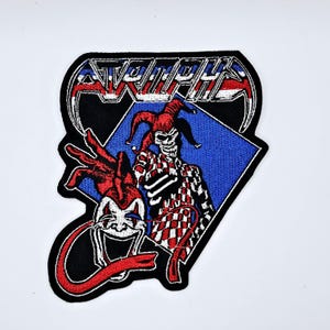 Op de afbeelding: Geborduurde patch met een narrenschedelontwerp. De patch heeft een zwarte rand en een blauwe diamantachtergrond. De nar draagt een rood-wit geruit kostuum en een rode narrenhoed. Het woord "ATROPHY" staat bovenaan.