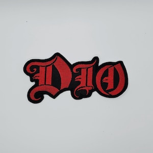 Può includere: Toppa ricamata con la scritta "DIO" in carattere gotico. Le lettere sono rosse con un bordo nero. La toppa è progettata per essere cucita o stirata su abiti o accessori.