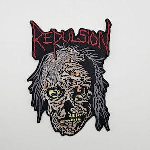 Może przedstawiać: Haftowana naszywka z motywem twarzy zombie i napisem "REPULSION" w kolorze czerwonym. Projekt przedstawia szczegółową, rozkładającą się twarz z wieloma oczami i żółto-zielonymi ustami na czarnym tle.