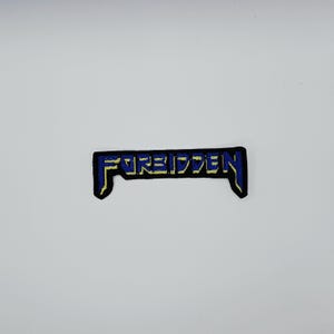 May include: A rectangular patch with the word "FORBIDDEN" embroidered in blue thread on a black background. The patch has a yellow border and a stylized font.