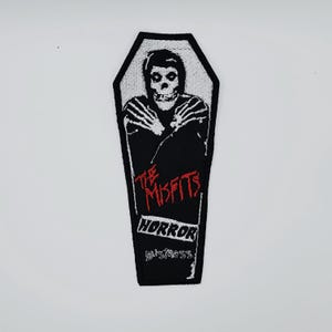 Puede incluir: Parche bordado en blanco y negro con forma de ataúd. Presenta una calavera y el texto "THE MISFITS HORROR" en rojo. Tema gótico.