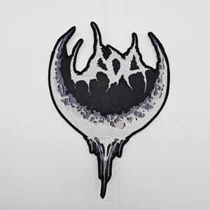 以下が含まれることがあります： ユニークなデザインの白黒パッチ。パッチは、テクスチャ加工されたグレーと白のボーダーが付いた、中央の黒い形状が特徴です。パッチの下部には滴るような効果があります。衣類やアクセサリーに適しています。