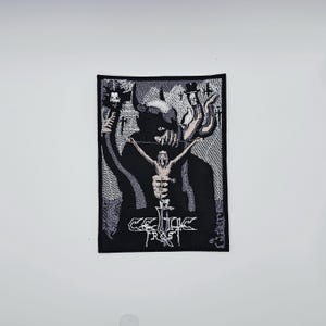May include: A black and white woven patch featuring a dark illustration of a horned figure holding a crucified person. The text "CELTIC FROST" is displayed in a stylized font at the bottom of the patch.