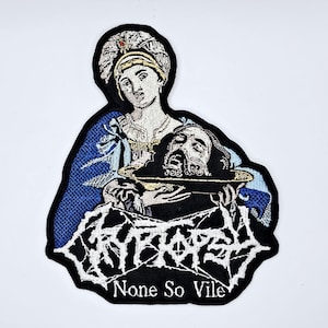 May include: Embroidered patch depicting a religious figure holding a platter with a severed head. The patch has a black border and features the text "CRYPTOSY" and "None So Vile" in white. The figure is shown in blue and gold.