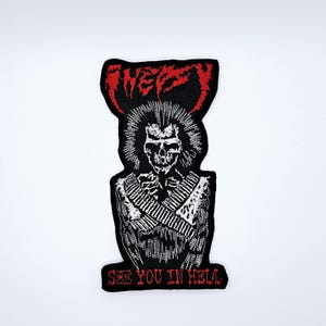 Op de afbeelding: Zwart geborduurde patch met een skeletfiguur met een hanenkam en een bandolier. De patch heeft het woord "FNEPZY" in rood bovenaan en "SEE YOU IN HELL" in rood onderaan. Het ontwerp staat op een witte achtergrond.