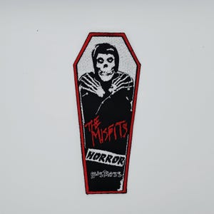 Op de afbeelding: Zwart-witte patch met een doodskistvormig ontwerp en een rode rand. Het heeft een skeletfiguur en de tekst "THE MISFITS HORROR business" in rood en wit.