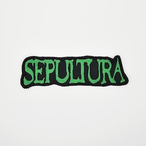 May include: A black patch with the word "SEPULTURA" embroidered in green, with a jagged border. The rectangular patch is designed to be sewn or ironed onto clothing or accessories. The design is simple and bold, suitable for fans of the band.