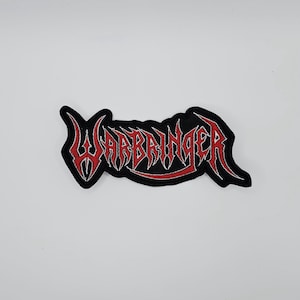 May include: A black embroidered patch with the word "WARBRINGER" in red, stylized, gothic lettering. The patch has a black border and is likely for clothing or accessories.