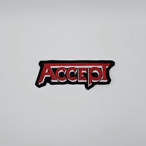 Op de afbeelding: Geborduurde patch met het woord "ACCEPT" in rood, wit omlijnd en met een zwarte rand. De patch heeft een vet, gestileerd lettertype, geschikt voor kleding of accessoires.