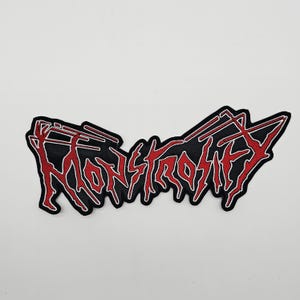Puede incluir: Un parche negro con la palabra "MONSTROSITY" en letras rojas estilizadas. El parche tiene un borde rojo y un fondo negro. El diseño es audaz y llamativo, adecuado para chaquetas, bolsos u otras prendas.