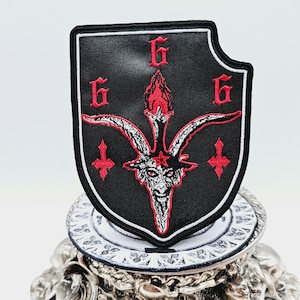 May include: Black embroidered patch featuring a red goat's head with horns, a star, and flames. The patch has three red "6"s surrounding the goat's head and two red upside down crosses.