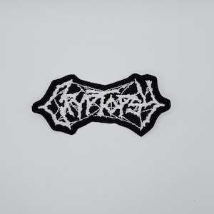 Op de afbeelding: Een zwart-wit geborduurde patch met het woord "ENTOMBED" in een gestileerd, gotisch lettertype. De patch heeft een unieke, onregelmatige vorm en is waarschijnlijk ontworpen voor kleding of accessoires.