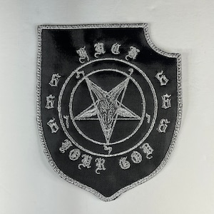Op de afbeelding: Zwarte patch met een zilveren geborduurd pentagram in een cirkel met de woorden "YOUR GOD" en "666" eromheen.