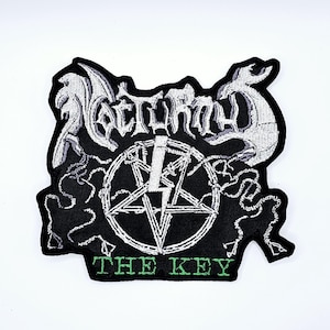 May include: Black embroidered patch with the word "Nocturnus" in a gothic font, a pentagram, and the text "THE KEY" in green. The patch has a detailed design with white and gray accents.