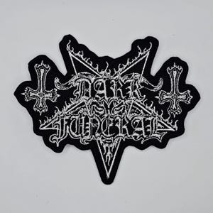 May include: A black and white embroidered patch featuring the words "DARK FUNERAL" in a gothic style, set within a pentagram and flanked by inverted crosses. The patch has a jagged border.