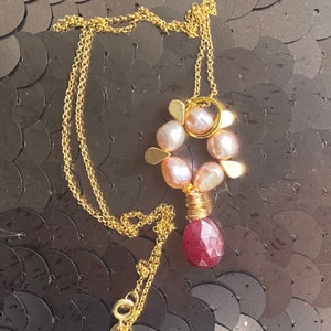Puede incluir: Un collar de cadena dorada con un colgante que presenta un grupo de perlas rosadas y una piedra preciosa roja rubí.