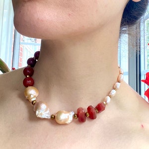 May include: A layered necklace featuring red, orange, and white beads. The necklace is crafted from natural stones and pearls.