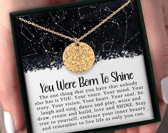 May include: A gold-coloured necklace with a round pendant showing a star map design. The pendant hangs on a delicate chain, presented in a black box with the text "You Were Born To Shine". The box has a starry background.