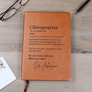May include: A brown leather-bound notebook with the word "Chiropractor" and its definition printed on the cover. The notebook includes the name "Dr. Johnson" in script. A bookmark is attached.