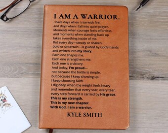 Può includere: Un diario in pelle marrone con il testo "I AM A WARRIOR" e una poesia stampata sulla copertina. Il diario ha un segnalibro a nastro ed è circondato da una penna, occhiali e una carta.